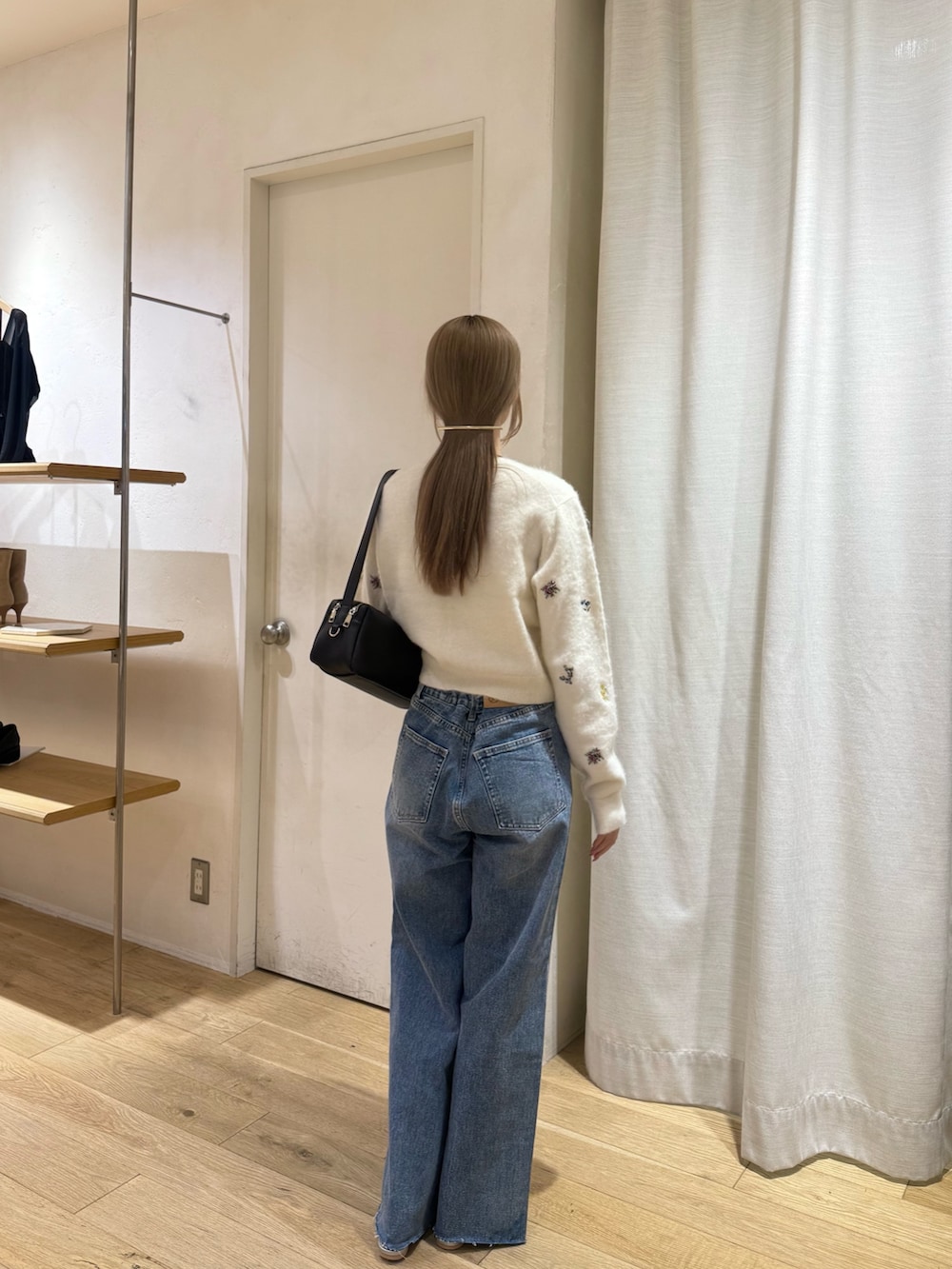 ホワイト系のカーディガン/ボレロ、ブラック系のショルダーバッグ、ブルー系のデニムパンツを着用したレディースの秋コーディネートの2枚目の写真