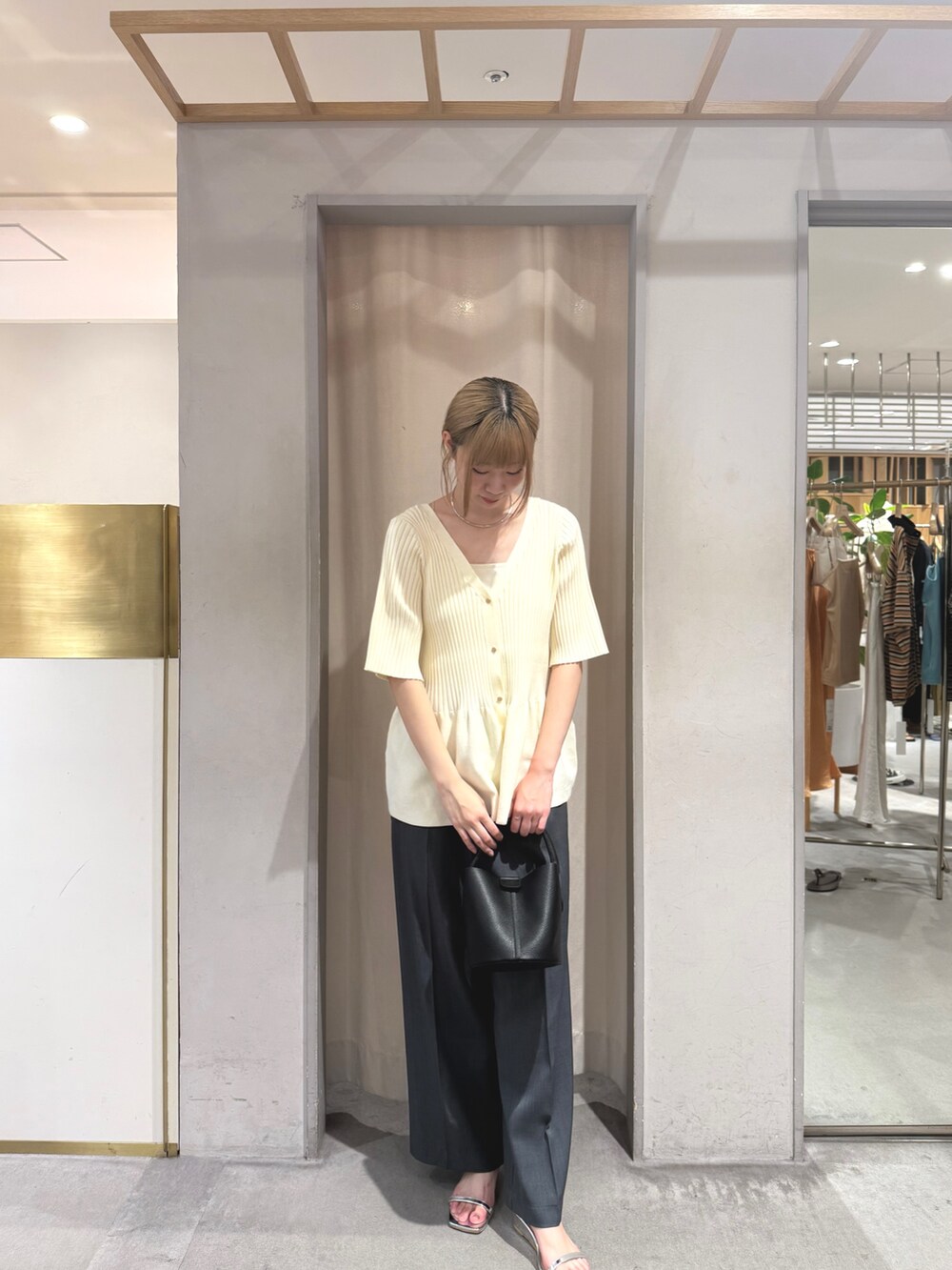 ホワイト系のニット/セーター、ブラック系のトートバッグ、グレー系のスラックスを着用したレディースの夏コーディネートの2枚目の写真