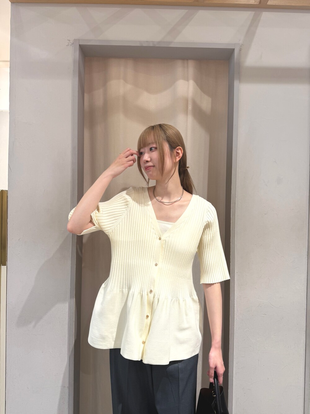 ホワイト系のニット/セーター、ブラック系のトートバッグ、グレー系のスラックスを着用したレディースの夏コーディネートの3枚目の写真