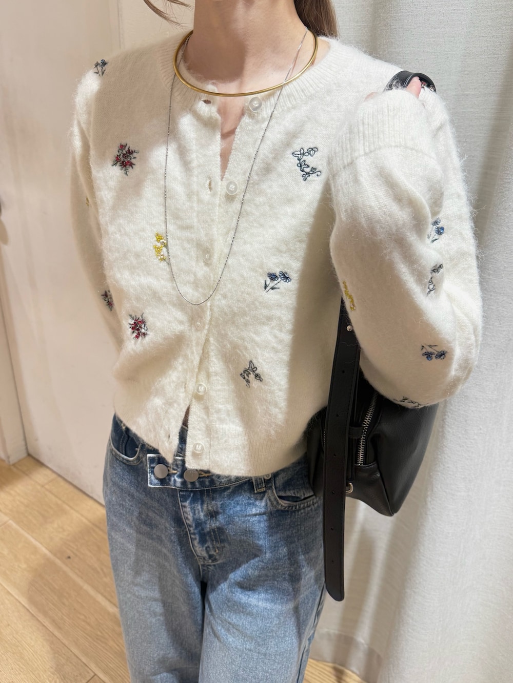 ホワイト系のカーディガン/ボレロ、ブラック系のショルダーバッグ、ブルー系のデニムパンツを着用したレディースの秋コーディネートの4枚目の写真