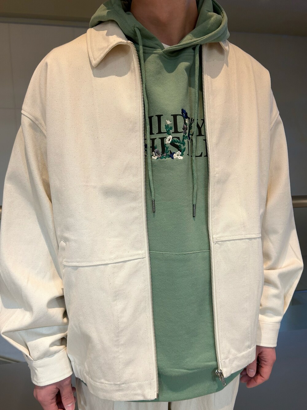 ホワイト系のデニムジャケット、グリーン系のパーカー、ホワイト系のデニムパンツを着用したメンズの春コーディネートの3枚目の写真