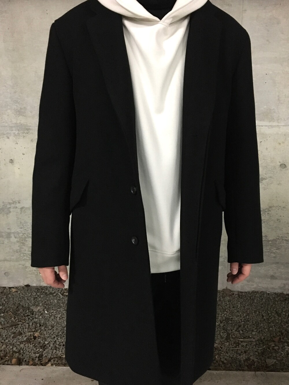 ブラック系のニット/セーター、ホワイト系のパーカー、ブラック系のチェスターコートを着用したメンズの冬コーディネートの3枚目の写真