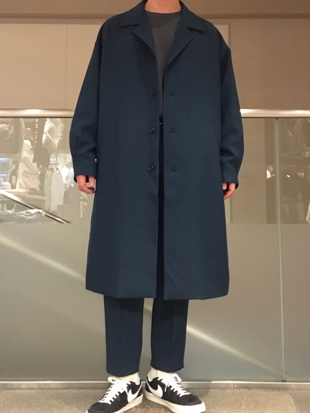 グリーン系のステンカラーコート、グレー系のTシャツ/カットソー、グリーン系のその他パンツを着用したメンズの春コーディネートの2枚目の写真