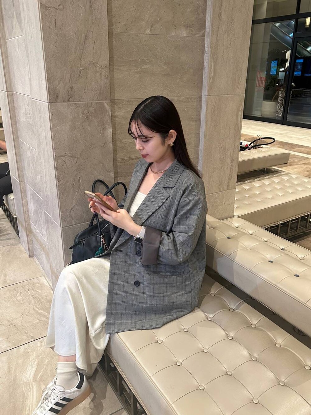 ブラック系のショルダーバッグ、ホワイト系のスカート、グレー系のテーラードジャケットを着用したレディースの秋コーディネートの2枚目の写真