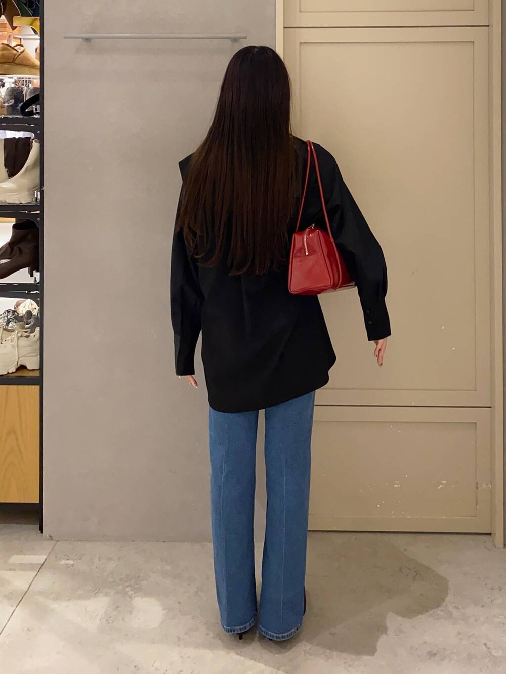 レッド系のボストンバッグ、ブラック系のブーツ、ブルー系のデニムパンツを着用したレディースの秋コーディネートの2枚目の写真