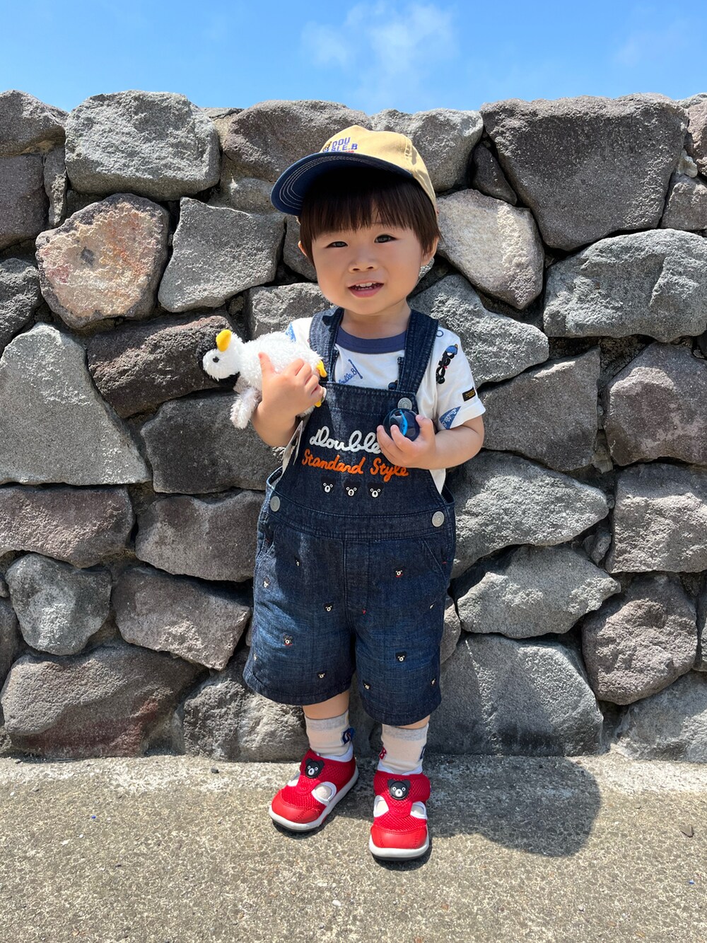 ホワイト系のTシャツ/カットソー、ブルー系のオールインワン・サロペット、ベージュ系のキャップを着用したキッズの夏コーディネートの2枚目の写真