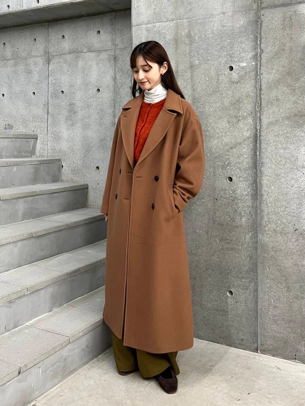 イエロー系のチェスターコート、ベージュ系のその他パンツ、オレンジ系のカーディガン/ボレロを着用したレディースの冬コーディネートの4枚目の写真