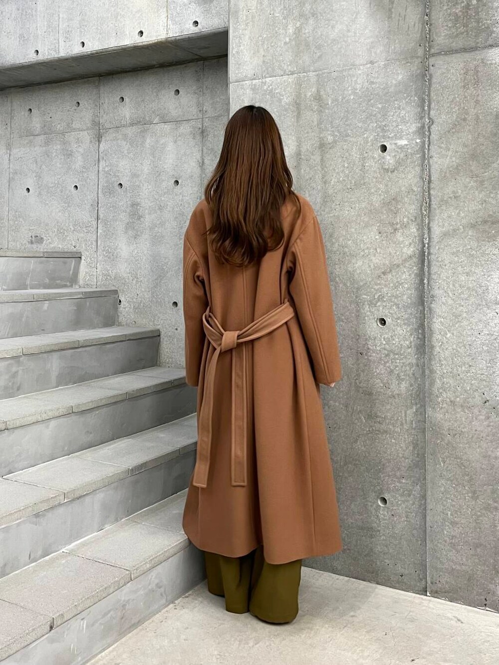 イエロー系のチェスターコート、ベージュ系のその他パンツ、オレンジ系のカーディガン/ボレロを着用したレディースの冬コーディネートの5枚目の写真