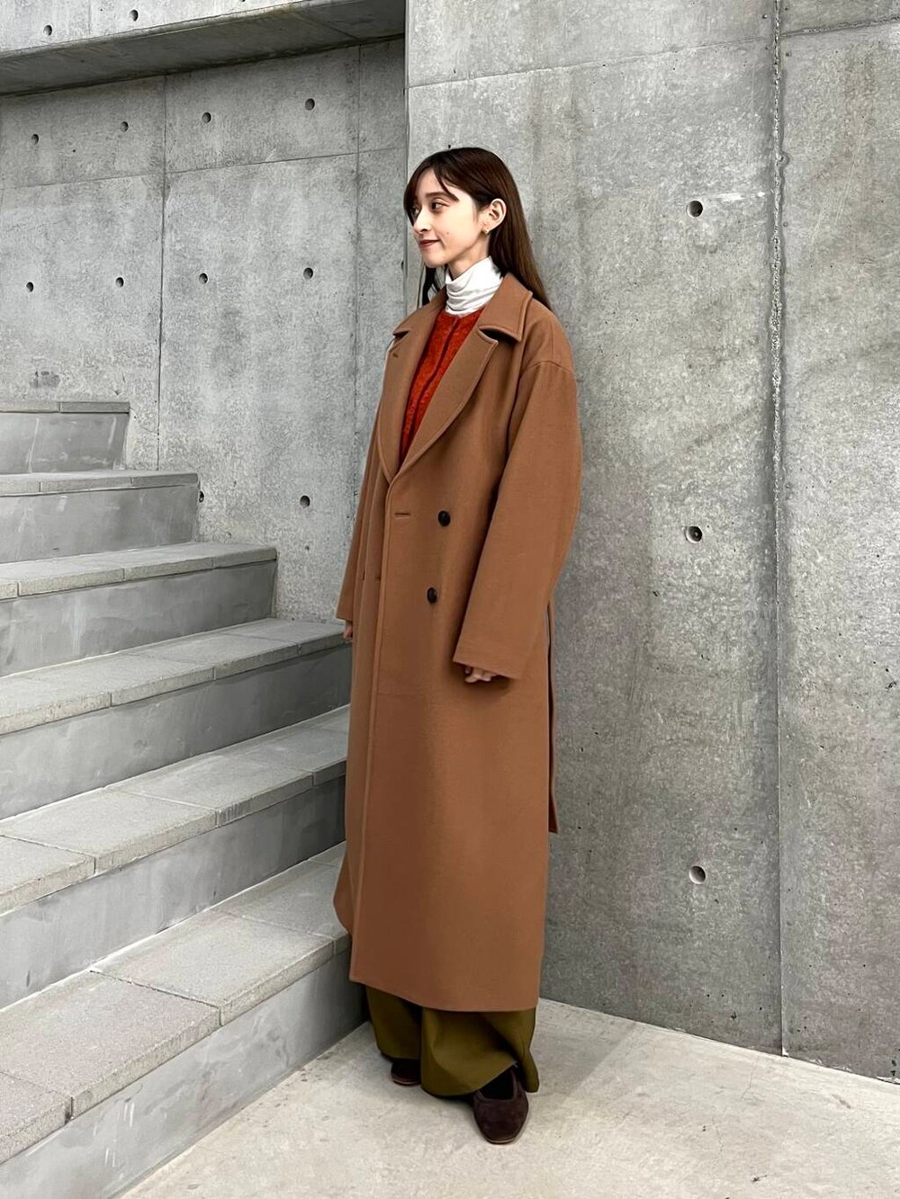 イエロー系のチェスターコート、ベージュ系のその他パンツ、オレンジ系のカーディガン/ボレロを着用したレディースの冬コーディネートの2枚目の写真