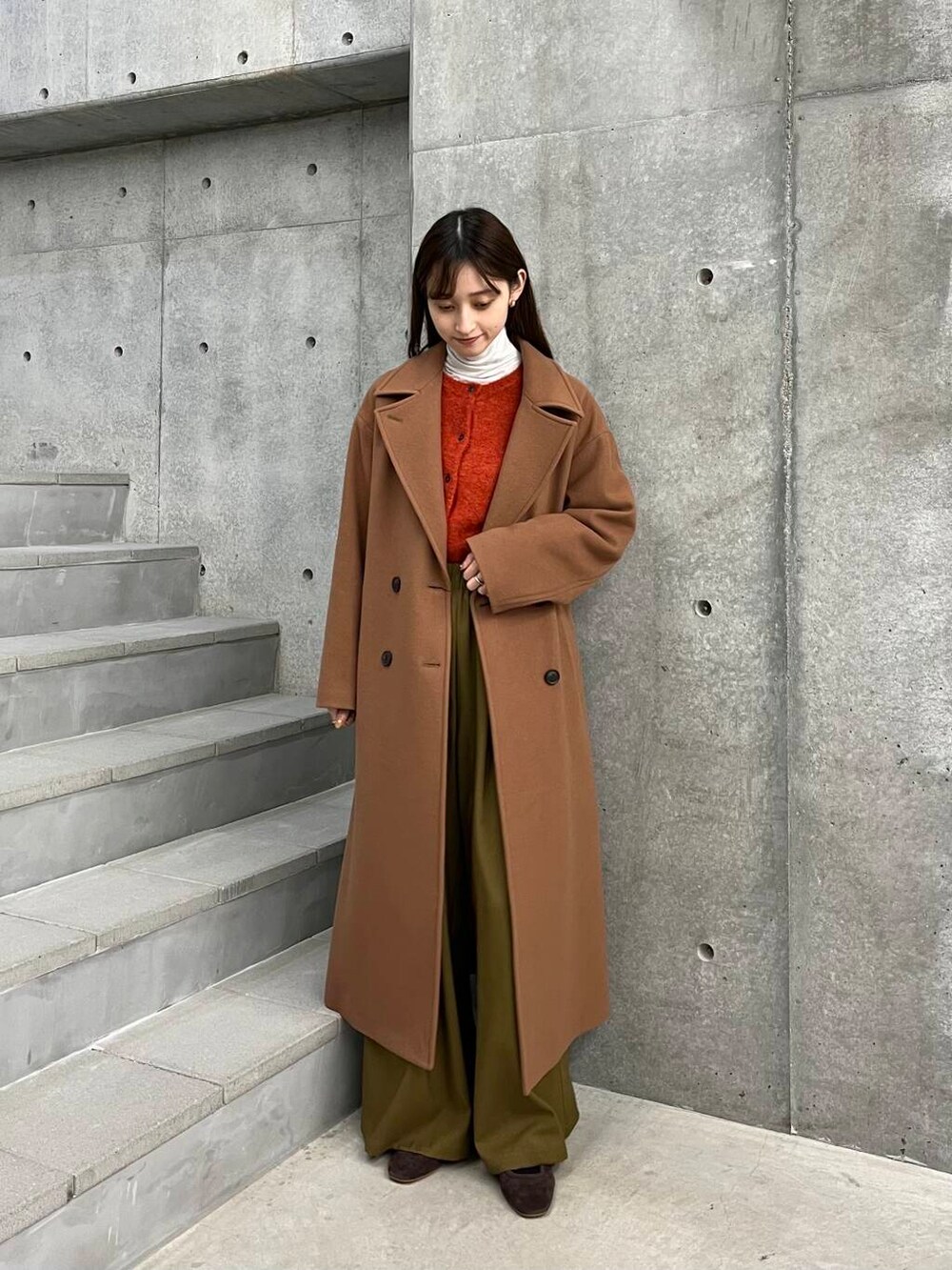 イエロー系のチェスターコート、ベージュ系のその他パンツ、オレンジ系のカーディガン/ボレロを着用したレディースの冬コーディネートの3枚目の写真