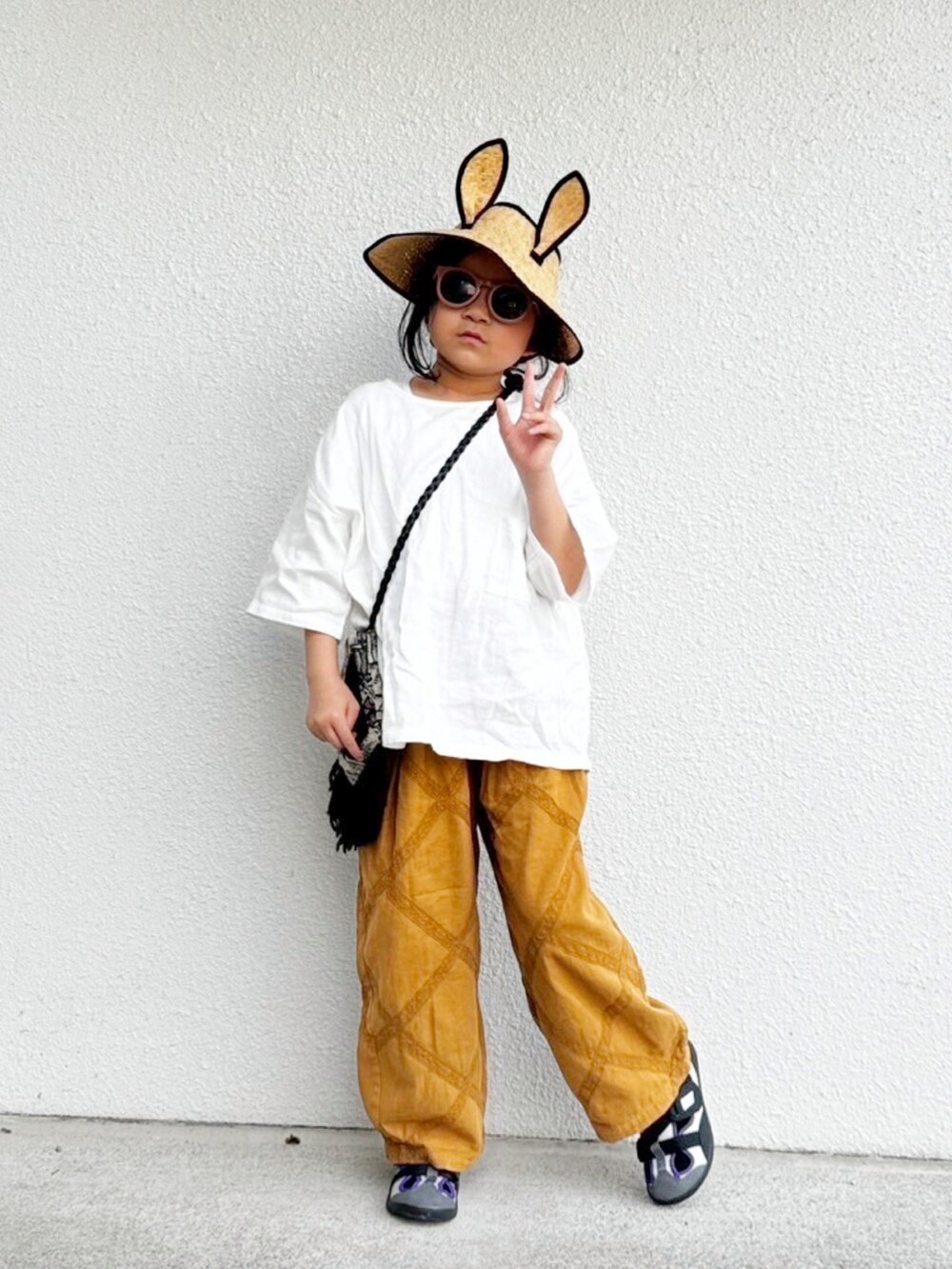 ホワイト系のトップス、ベージュ系のパンツ、ブラック系のバッグを着用したキッズの夏コーディネートの2枚目の写真