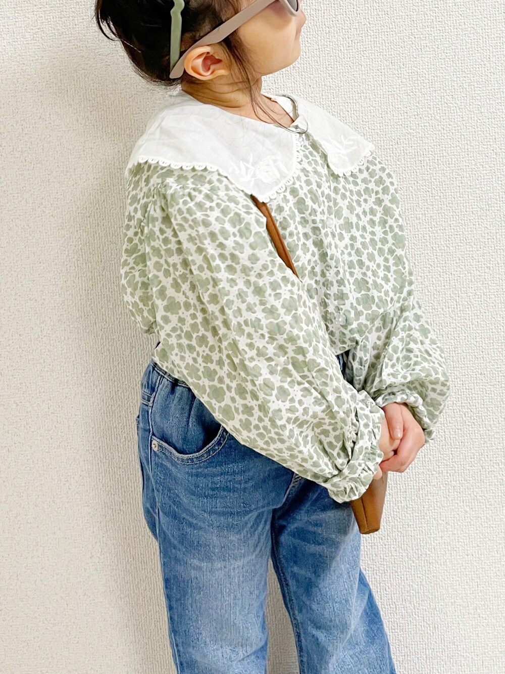 グリーン系のトップス、ブラウン系のショルダーバッグ、ブルー系のデニムパンツを着用したキッズの春コーディネートの3枚目の写真