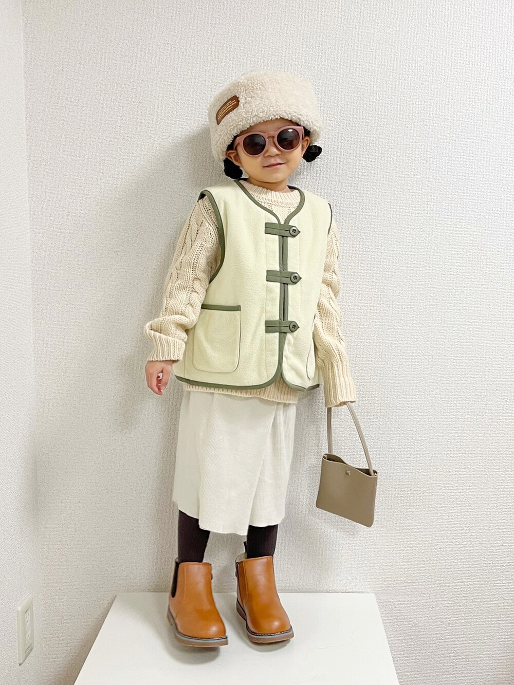 グリーン系のベスト、ホワイト系のニット/セーター、ホワイト系のスカートを着用したキッズの秋コーディネートの2枚目の写真