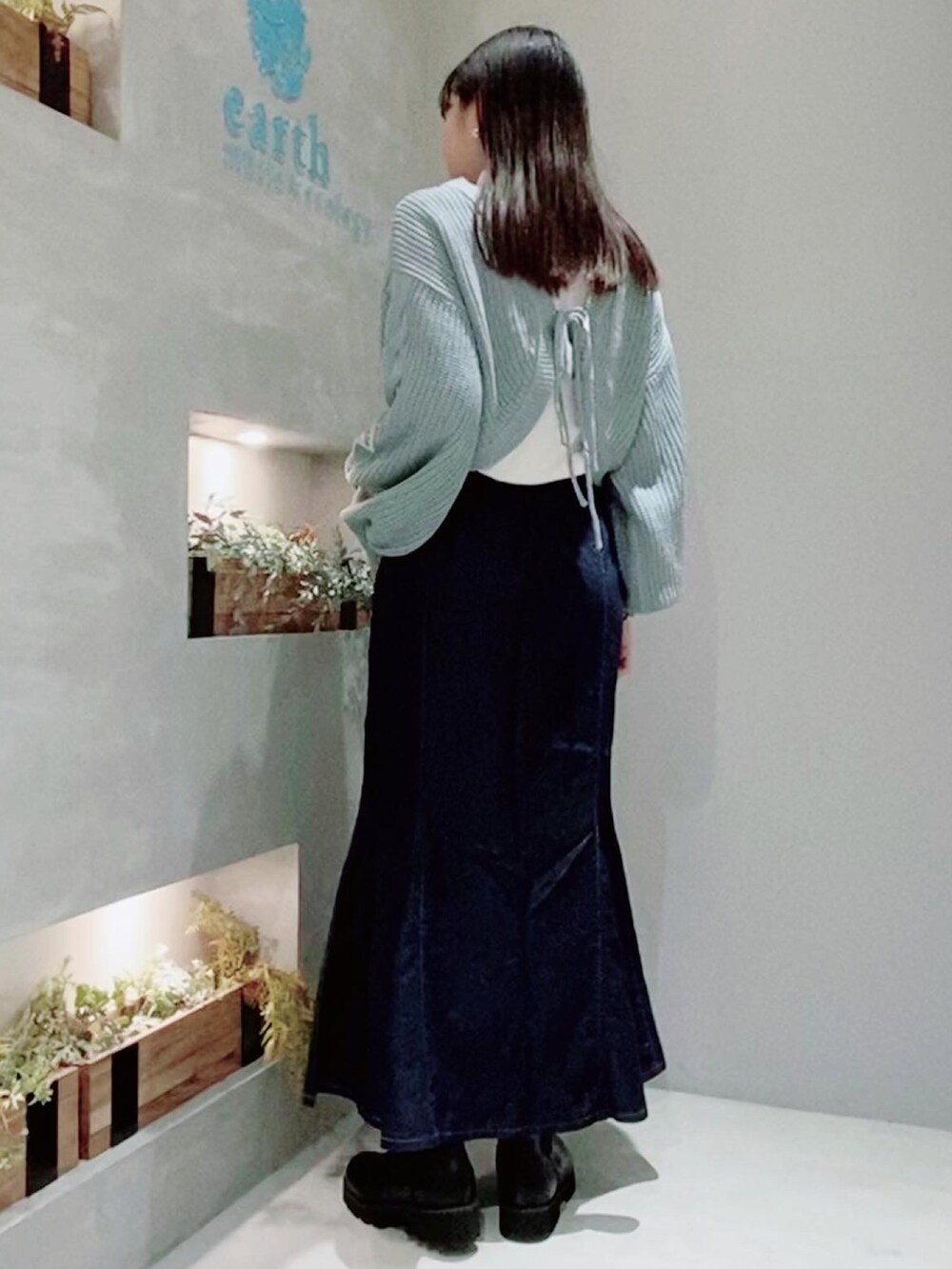 ブルー系のデニムスカート、ブルー系のカーディガン/ボレロ、ブラック系のブーツを着用したレディースの冬コーディネートの2枚目の写真