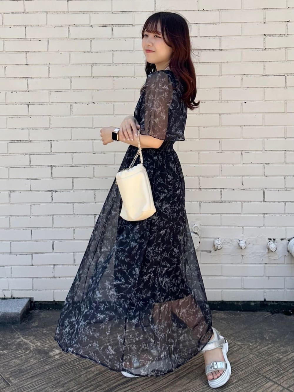 ブラック系のワンピース、ブラック系のサンダル、ホワイト系のハンドバッグを着用したレディースの夏コーディネートの3枚目の写真
