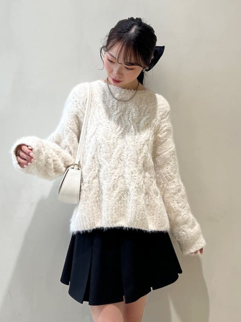 ホワイト系のニット/セーター、ブラック系のスカート、ブラウン系のブーツを着用したレディースの冬コーディネートの2枚目の写真