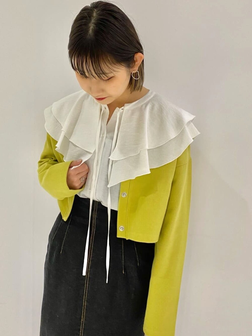 イエロー系のカーディガン/ボレロ、ブラック系のデニムスカート、ホワイト系のシャツ/ブラウスを着用したレディースの春コーディネートの2枚目の写真