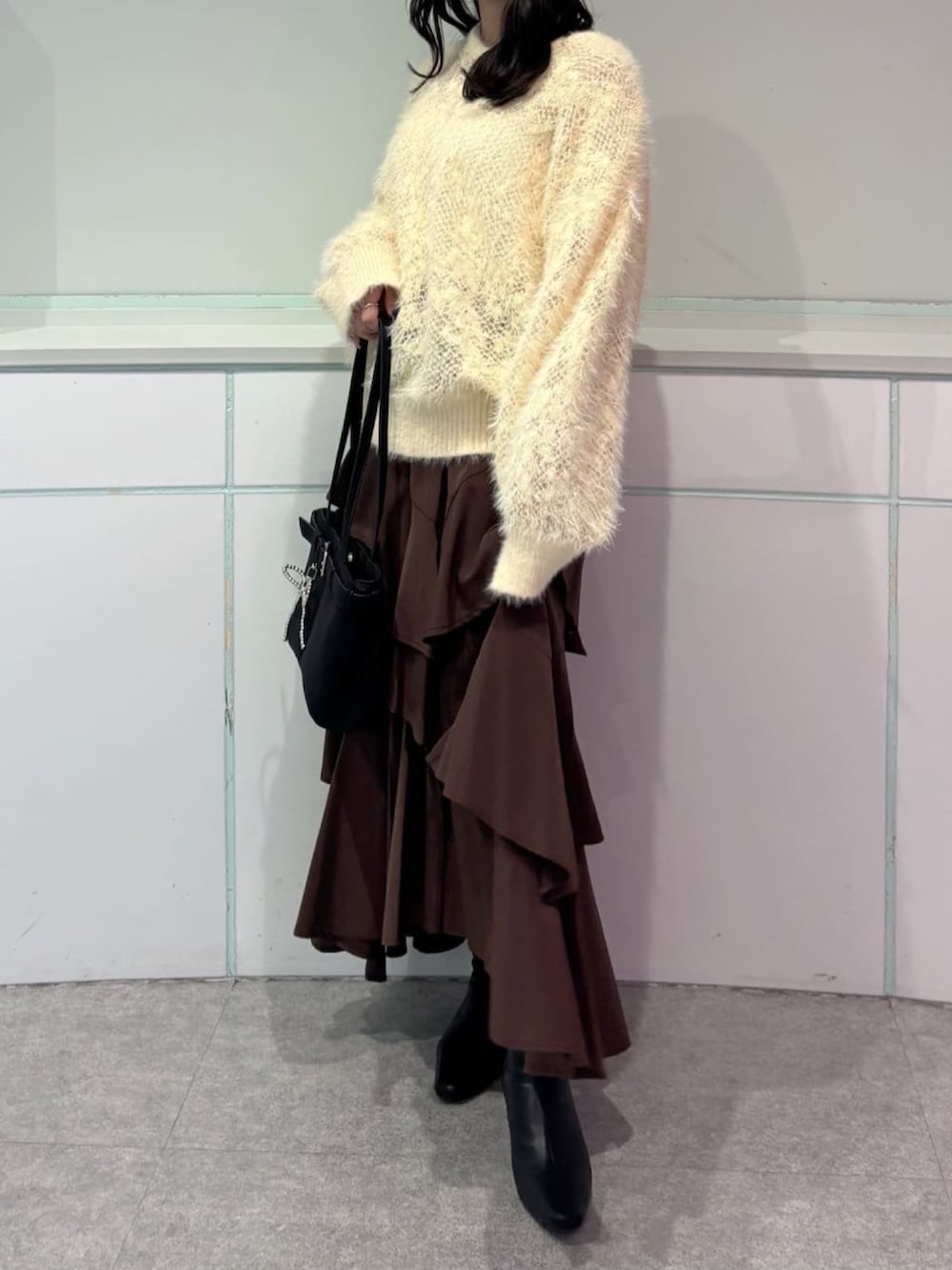 イエロー系のニット/セーター、ブラウン系のスカート、ブラック系のブーツを着用したレディースの秋コーディネートの2枚目の写真