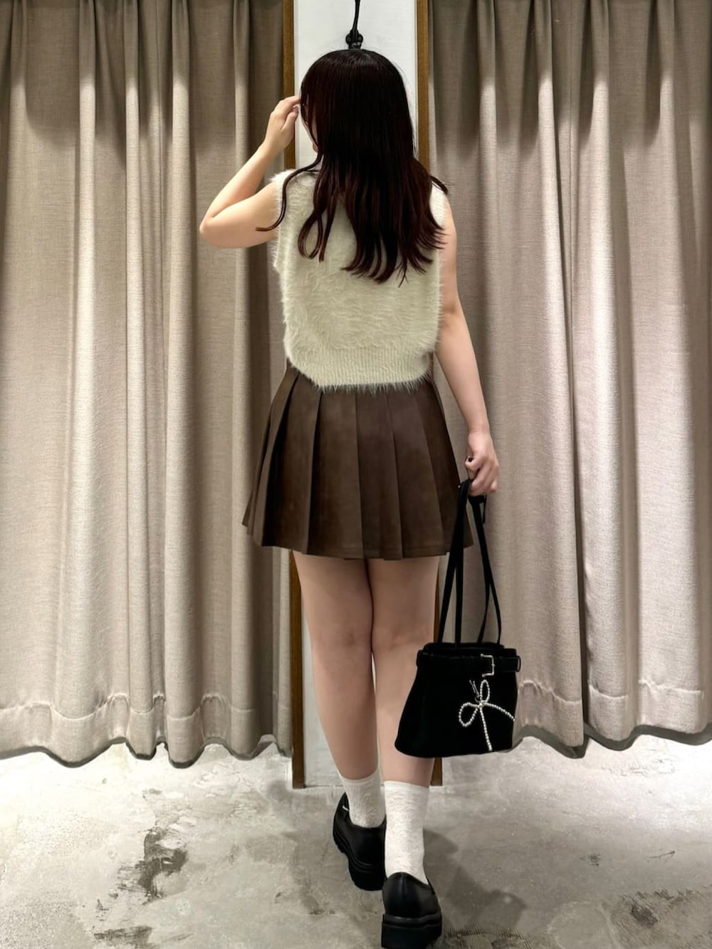 ホワイト系のベスト、ブラウン系のスカート、ブラック系のローファーを着用したレディースの秋コーディネートの3枚目の写真