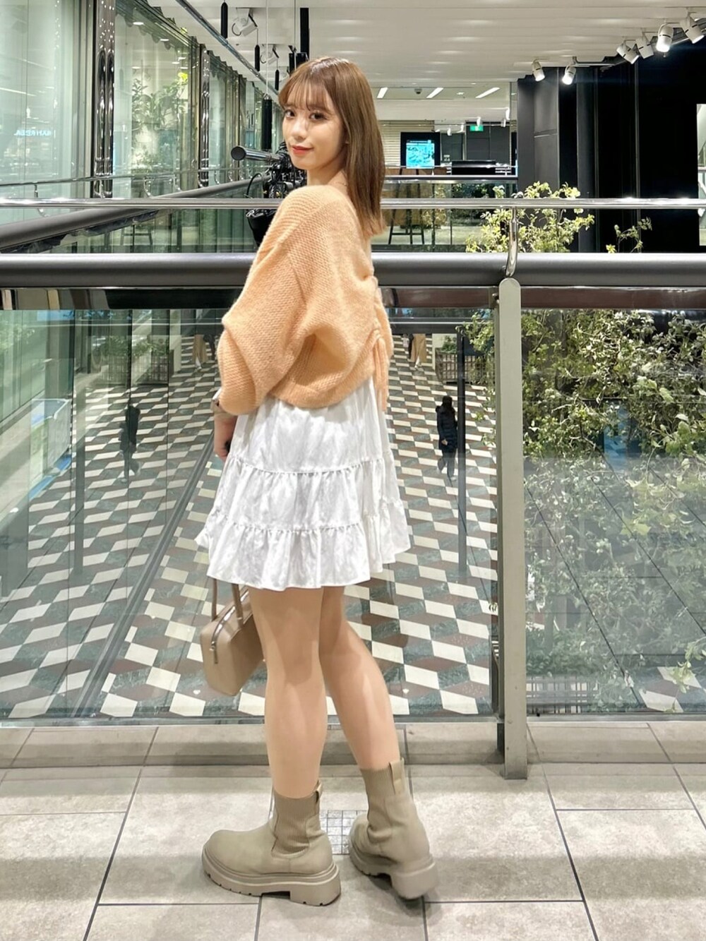 オレンジ系のニット/セーター、ホワイト系のスカートを着用したレディースの冬コーディネートの2枚目の写真