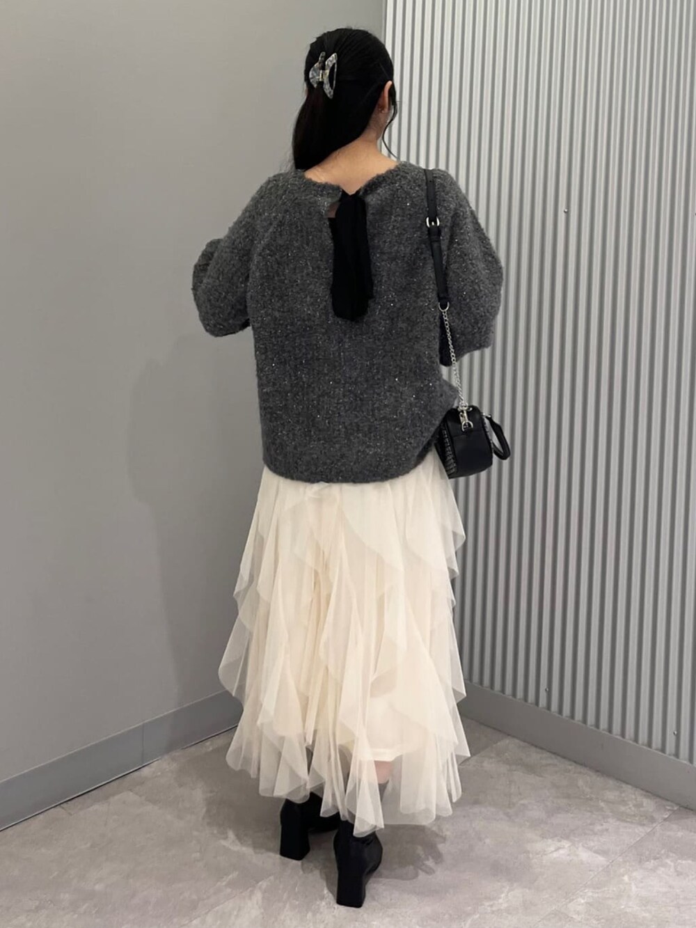 グレー系のニット/セーター、ホワイト系のスカート、ブラック系のショルダーバッグを着用したレディースの秋コーディネートの3枚目の写真