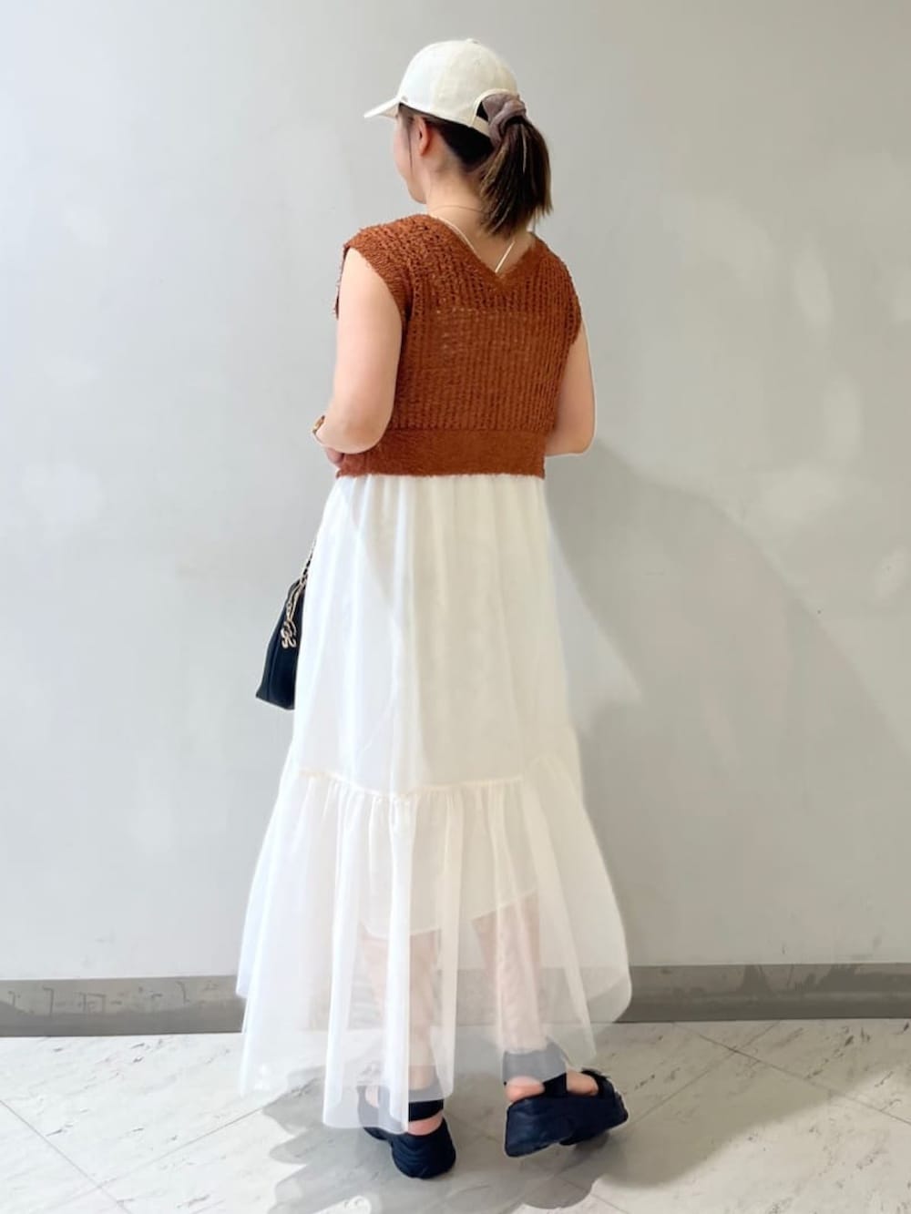 ブラック系のサンダル、ブラック系のハンドバッグ、オレンジ系のワンピースを着用したレディースの夏コーディネートの2枚目の写真