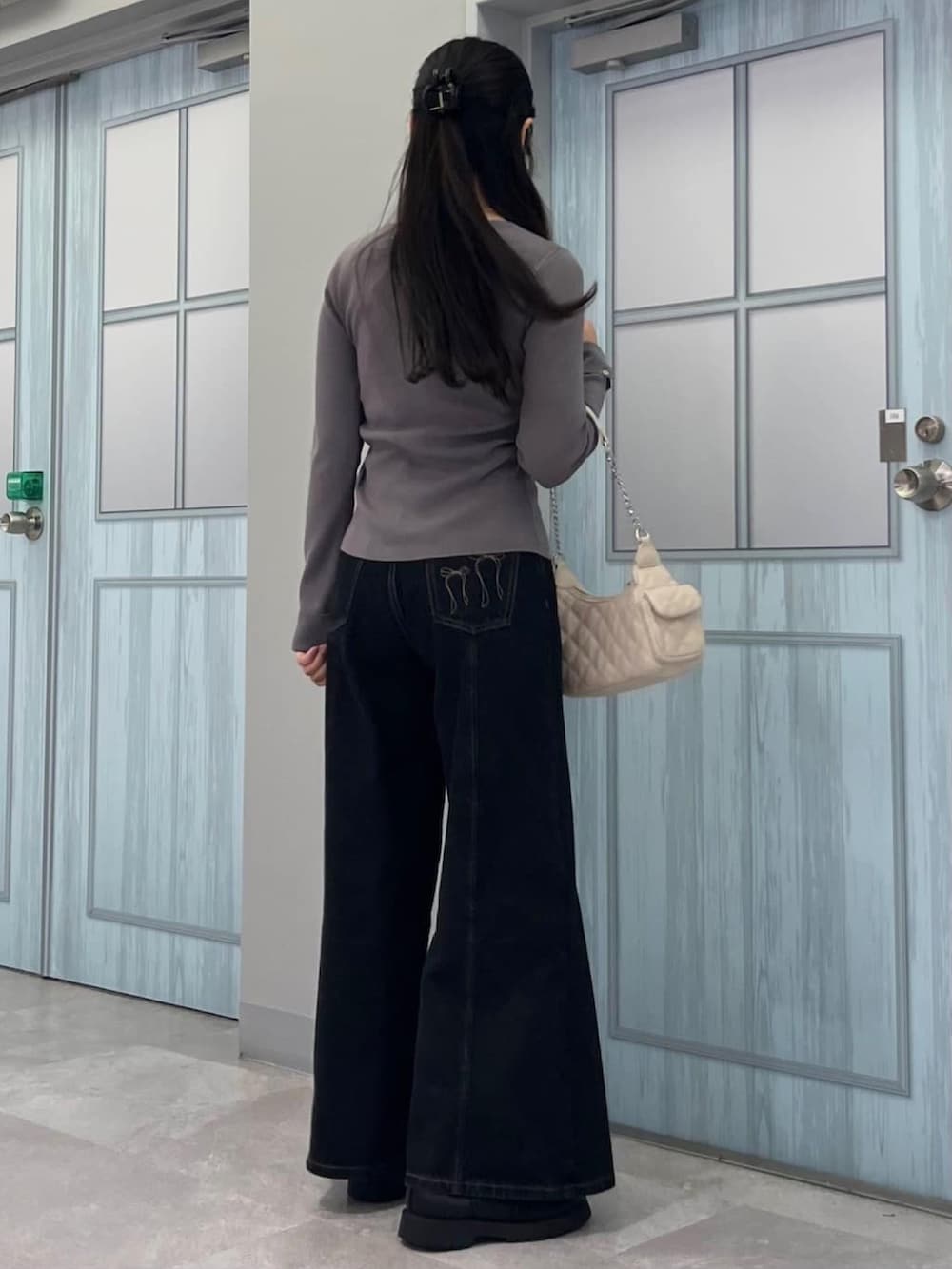 グレー系のニット/セーター、ブラック系のデニムパンツ、ホワイト系のショルダーバッグを着用したレディースの冬コーディネートの3枚目の写真