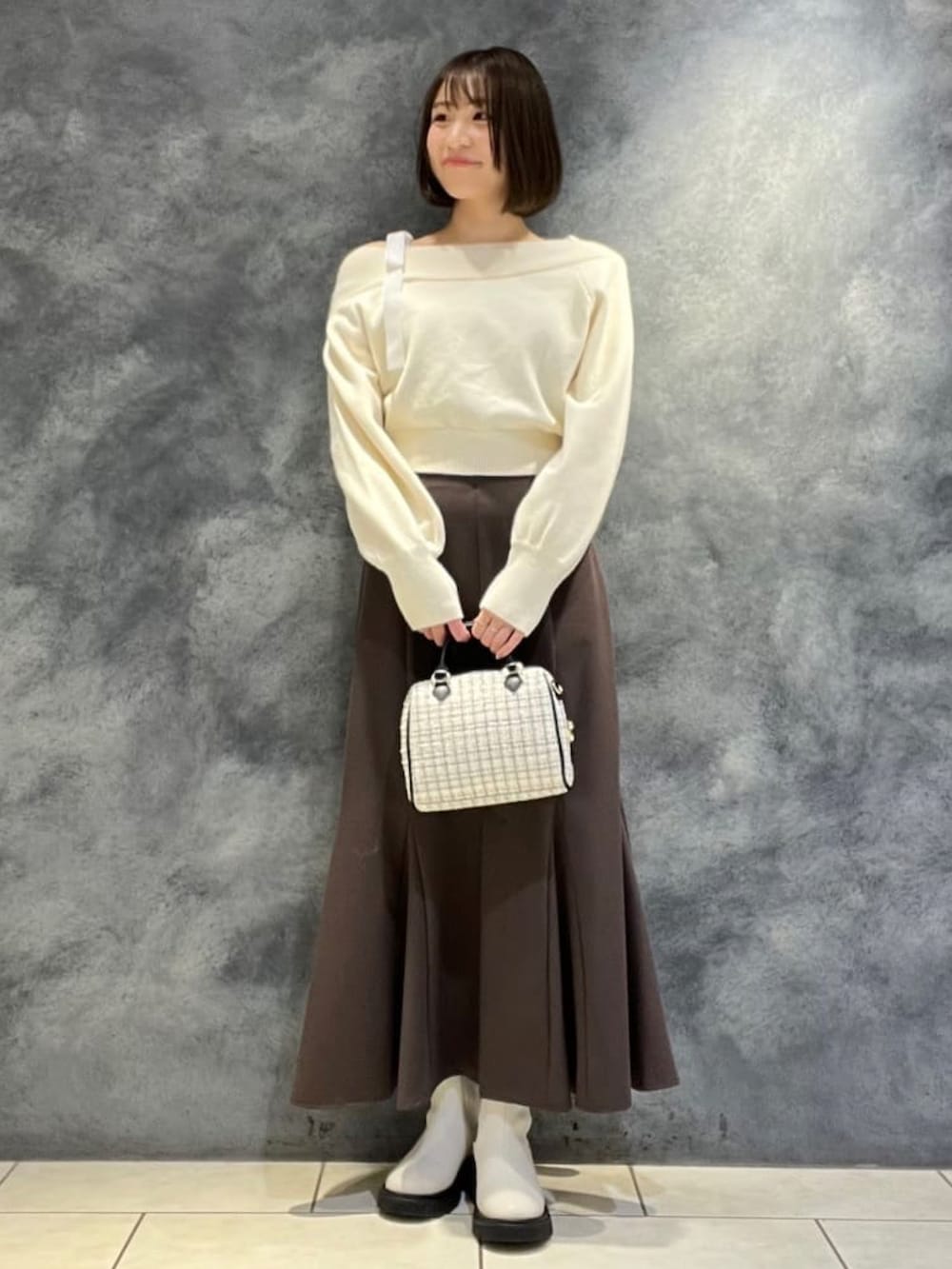 ホワイト系のニット/セーター、ホワイト系のボストンバッグ、ブラウン系のスカートを着用したレディースの冬コーディネートの2枚目の写真