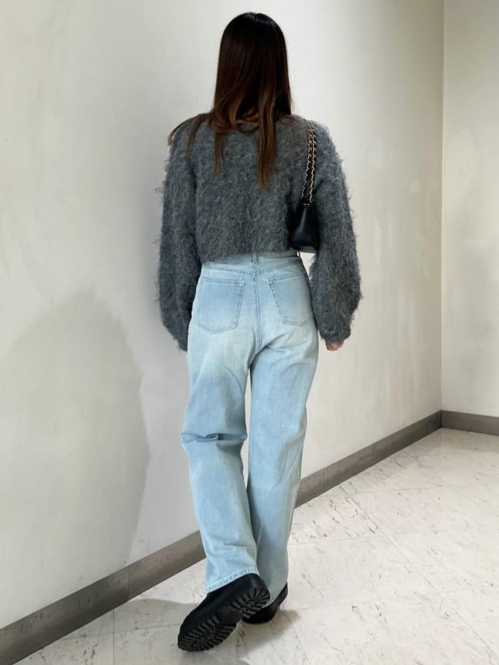 グレー系のニット/セーター、ブルー系のデニムパンツ、ブラック系のショルダーバッグを着用したレディースの冬コーディネートの2枚目の写真