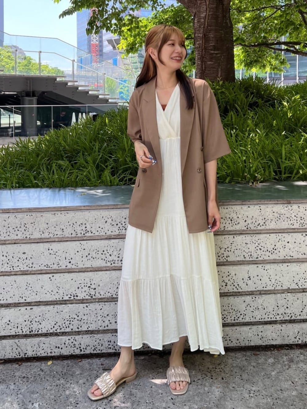 ホワイト系のテーラードジャケット、ベージュ系のワンピース、ゴールド系のサンダルを着用したレディースの夏コーディネートの2枚目の写真