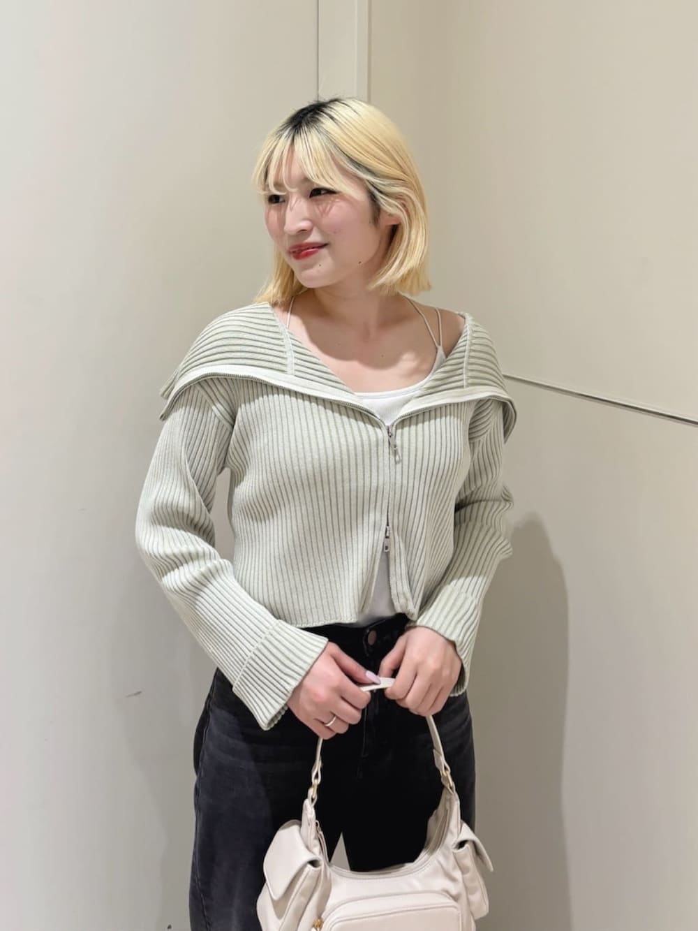 グリーン系のニット/セーター、ブラック系のデニムパンツ、ブラック系のハンドバッグを着用したレディースの春コーディネートの2枚目の写真