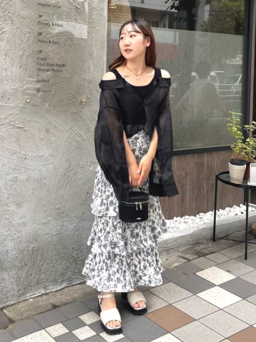 ブラック系のシャツ/ブラウス、ホワイト系のスカート、ホワイト系のサンダルを着用したレディースの夏コーディネートの2枚目の写真