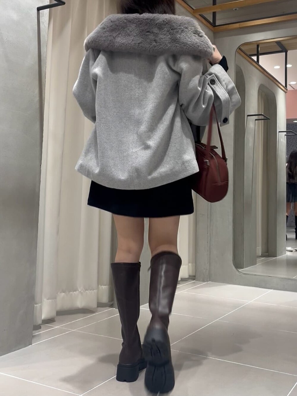 グレー系のピーコート、ブラック系のスカート、ブラック系のブーツを着用したレディースの秋コーディネートの2枚目の写真