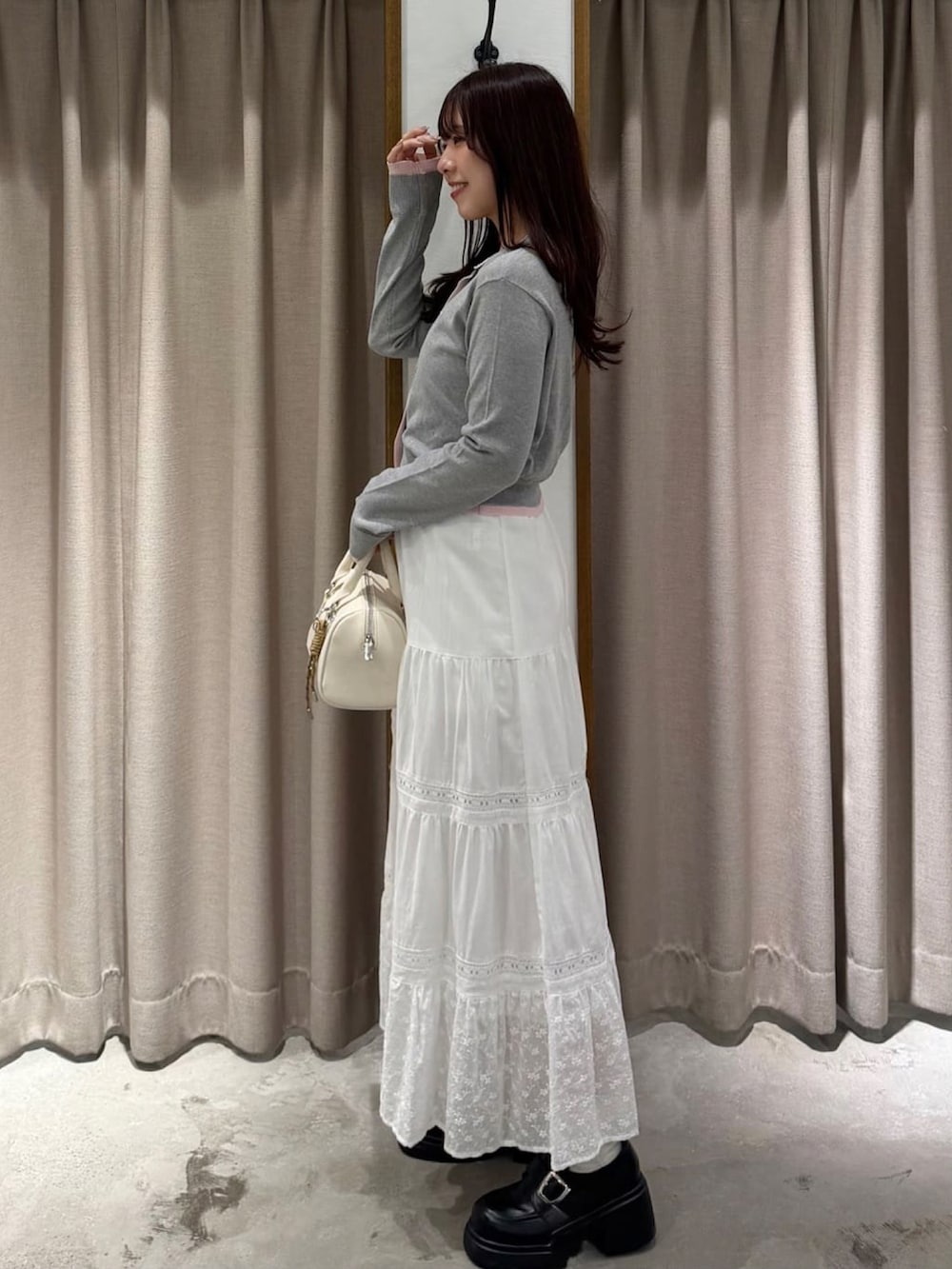 グレー系のカーディガン/ボレロ、ホワイト系のスカートを着用したレディースの春コーディネートの2枚目の写真