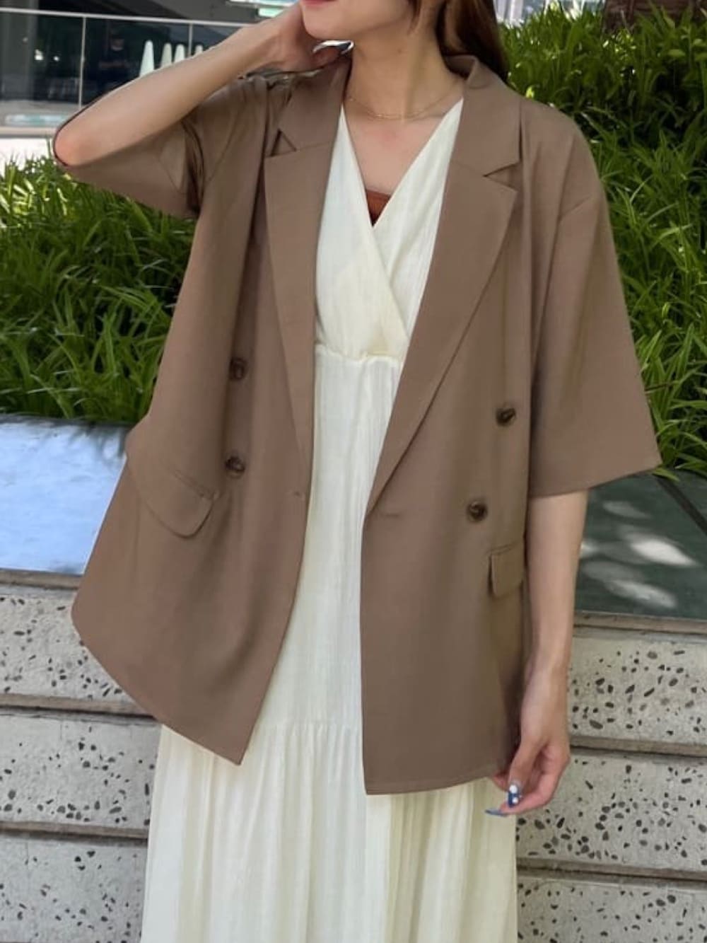 ホワイト系のテーラードジャケット、ベージュ系のワンピース、ゴールド系のサンダルを着用したレディースの夏コーディネートの3枚目の写真