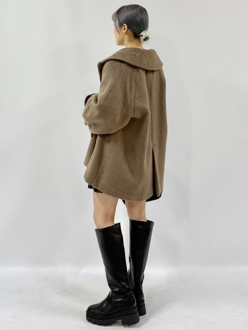 ブラック系のチェスターコート、ブラック系のスカート、ホワイト系のカーディガン/ボレロを着用したレディースの冬コーディネートの3枚目の写真