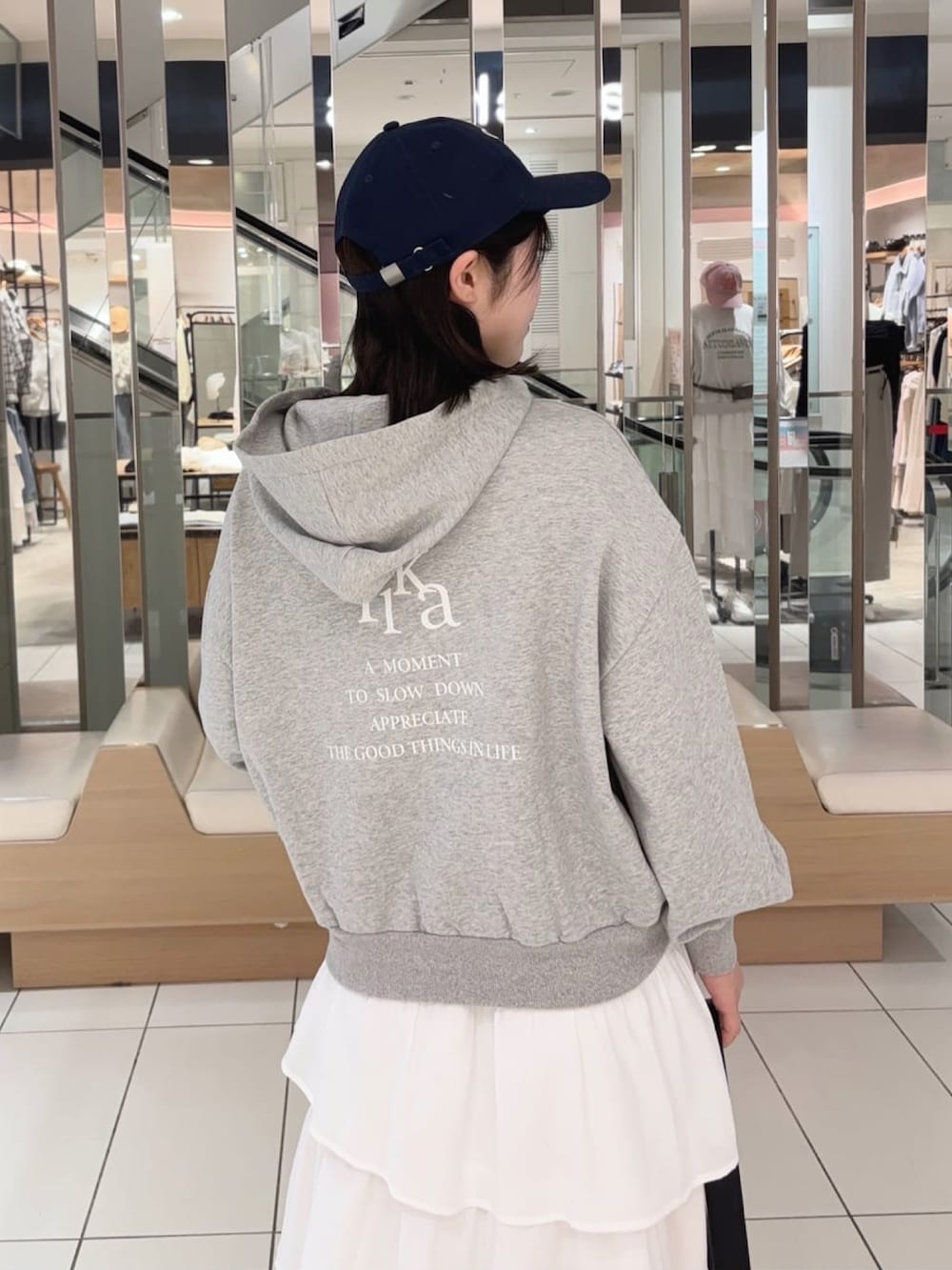 グレー系のパーカー、ホワイト系のスカート、ブラック系のショルダーバッグを着用したレディースの春コーディネートの3枚目の写真