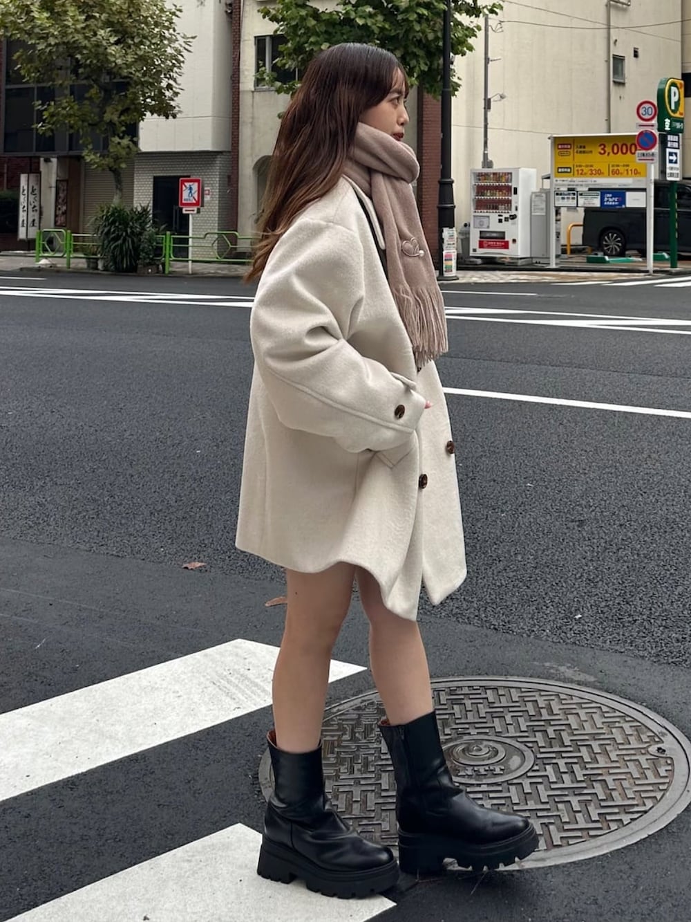 ホワイト系のチェスターコート、ブラック系のブーツ、ブラウン系のマフラーを着用したレディースの冬コーディネートの2枚目の写真