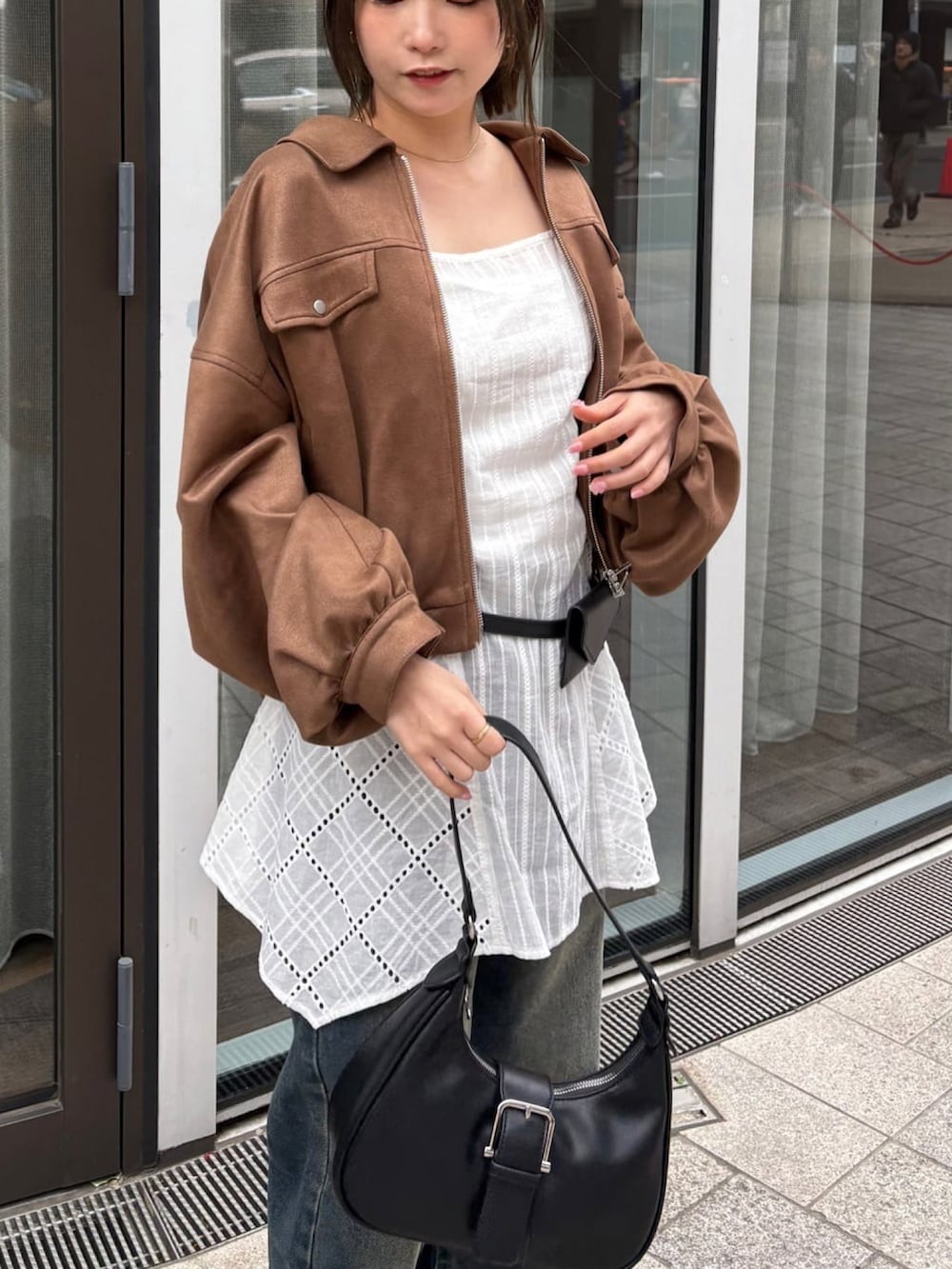 ブラウン系のブルゾン、ホワイト系のワンピース、ブルー系のデニムパンツを着用したレディースの春コーディネートの2枚目の写真