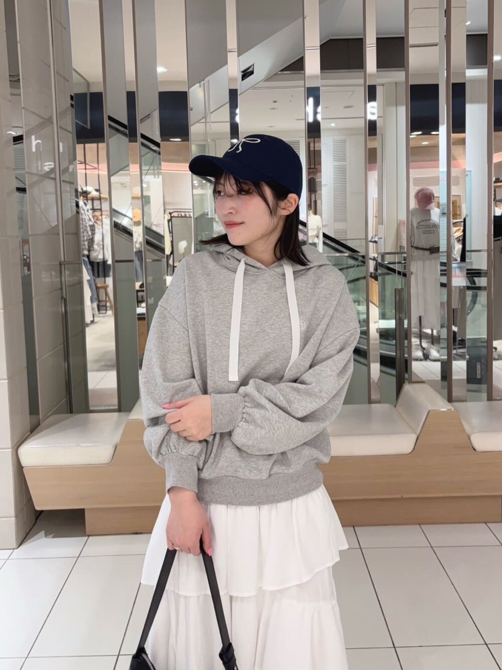 グレー系のパーカー、ホワイト系のスカート、ブラック系のショルダーバッグを着用したレディースの春コーディネートの2枚目の写真