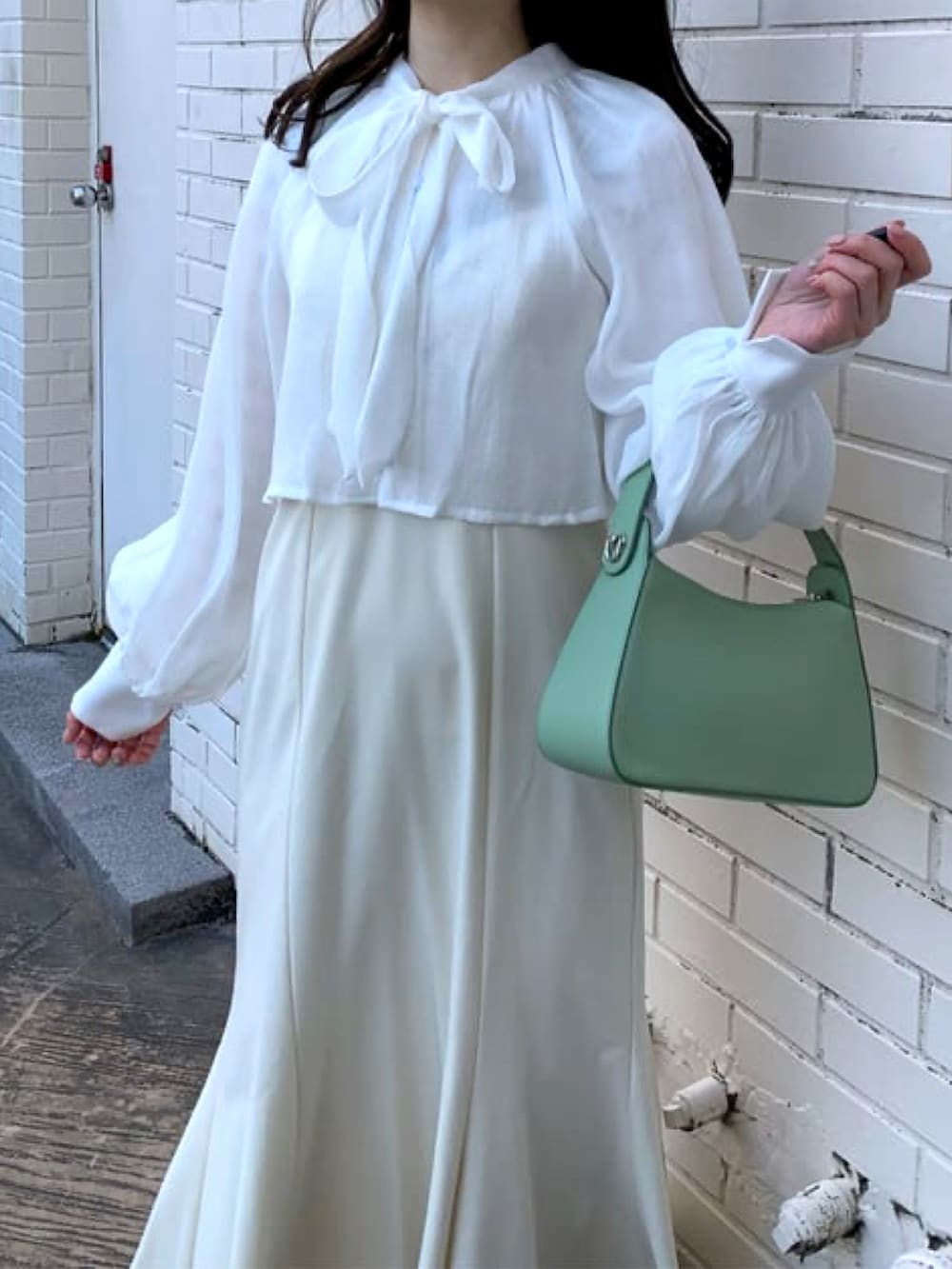 グリーン系のハンドバッグ、ホワイト系のワンピース、ホワイト系のブーツを着用したレディースの冬コーディネートの2枚目の写真