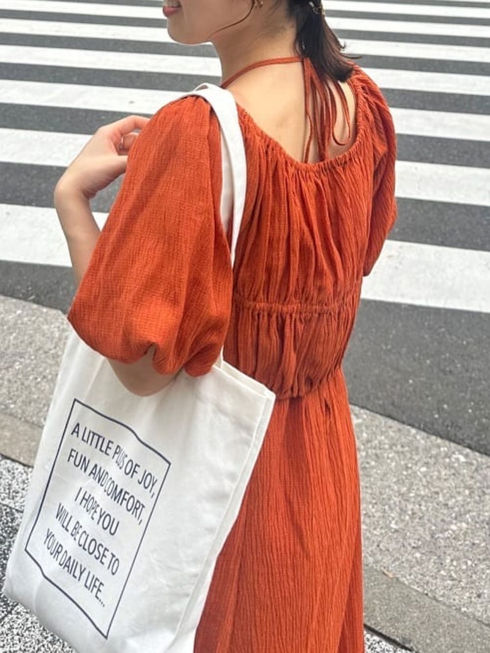 オレンジ系のワンピース、グレー系のサンダル、ホワイト系のトートバッグを着用したレディースの夏コーディネートの3枚目の写真