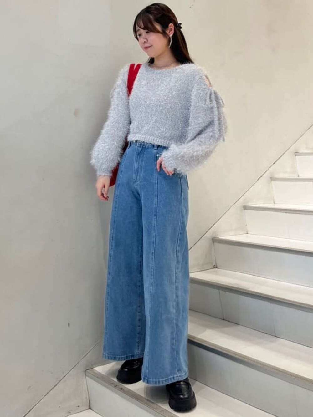 グレー系のニット/セーター、ブルー系のデニムパンツ、レッド系のトートバッグを着用したレディースの冬コーディネートの2枚目の写真