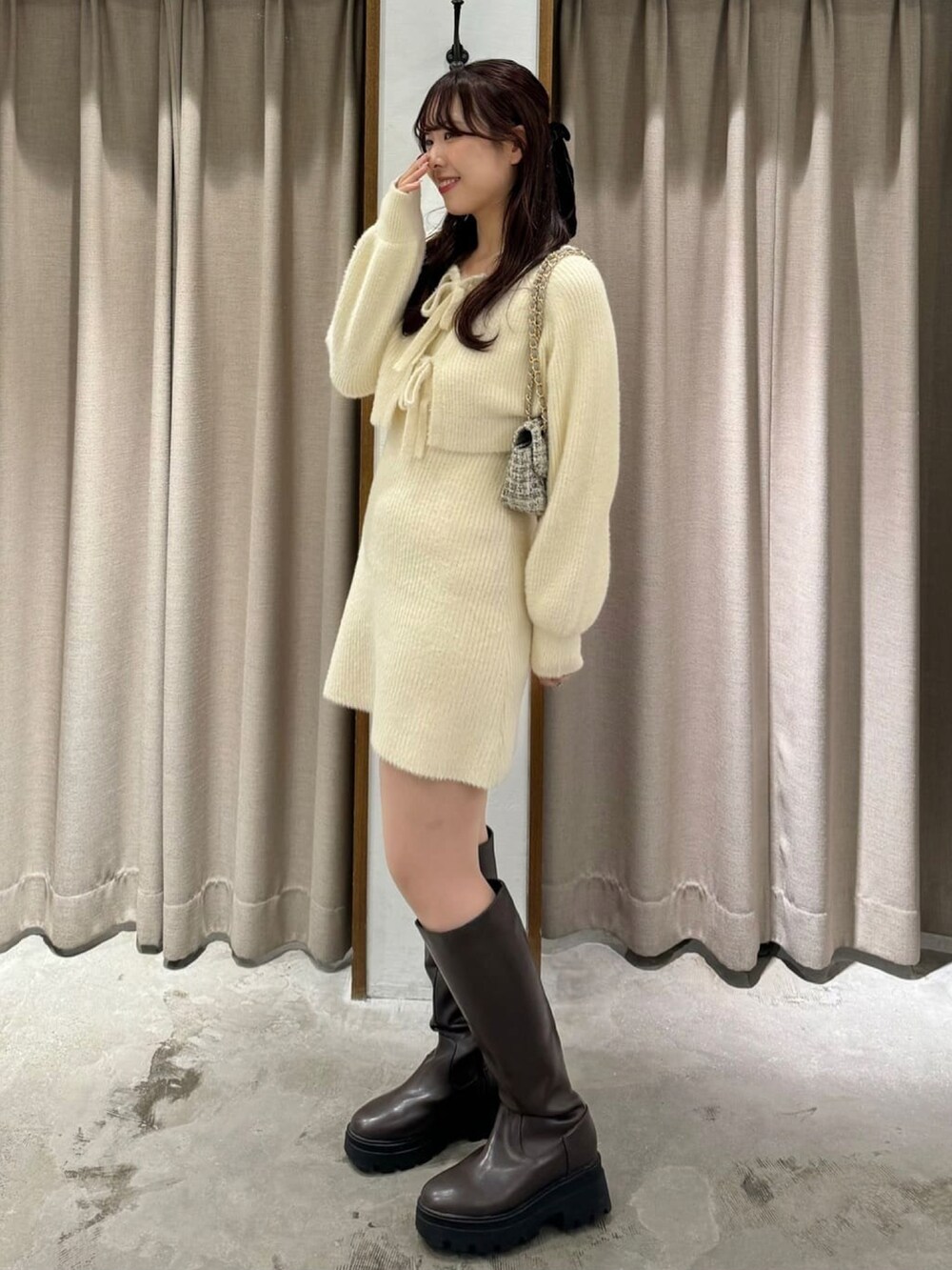 ホワイト系のワンピース、ホワイト系のショルダーバッグ、ブラウン系のブーツを着用したレディースの冬コーディネートの2枚目の写真