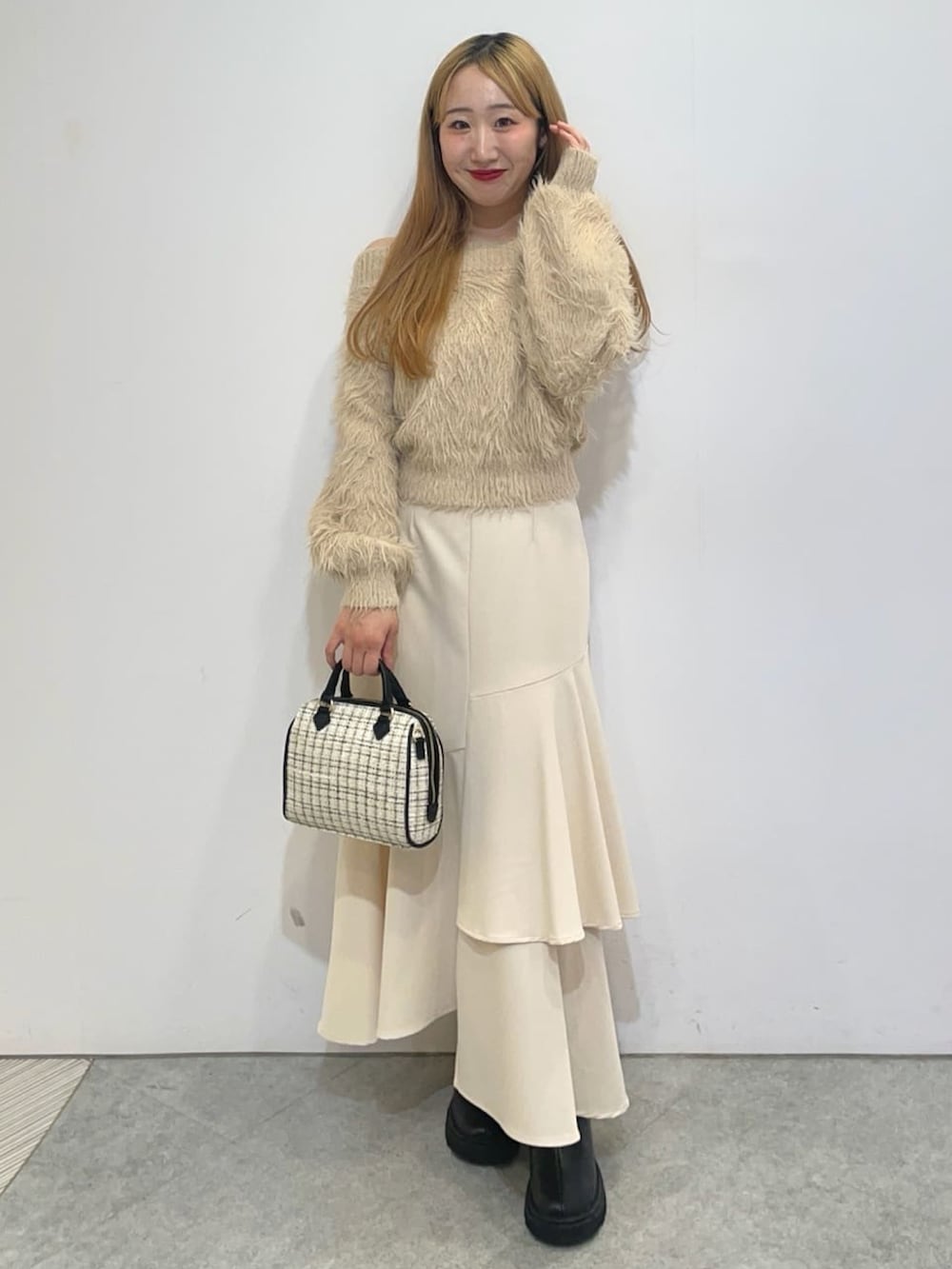 ベージュ系のニット/セーター、ホワイト系のスカート、ホワイト系のボストンバッグを着用したレディースの冬コーディネートの2枚目の写真