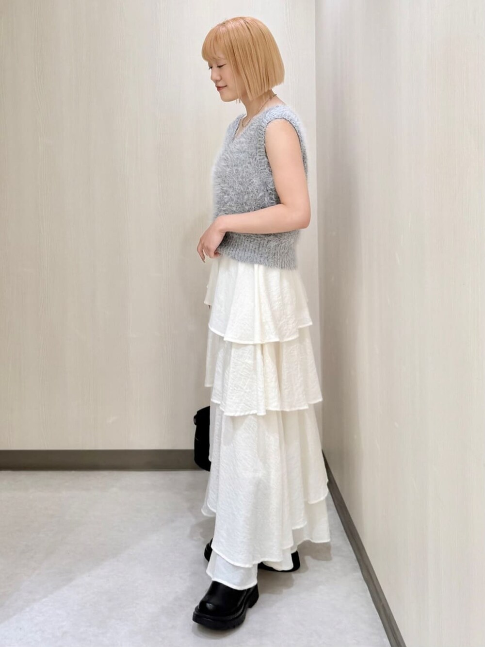 グレー系のベスト、ホワイト系のスカート、ベージュ系のショルダーバッグを着用したレディースの秋コーディネートの2枚目の写真