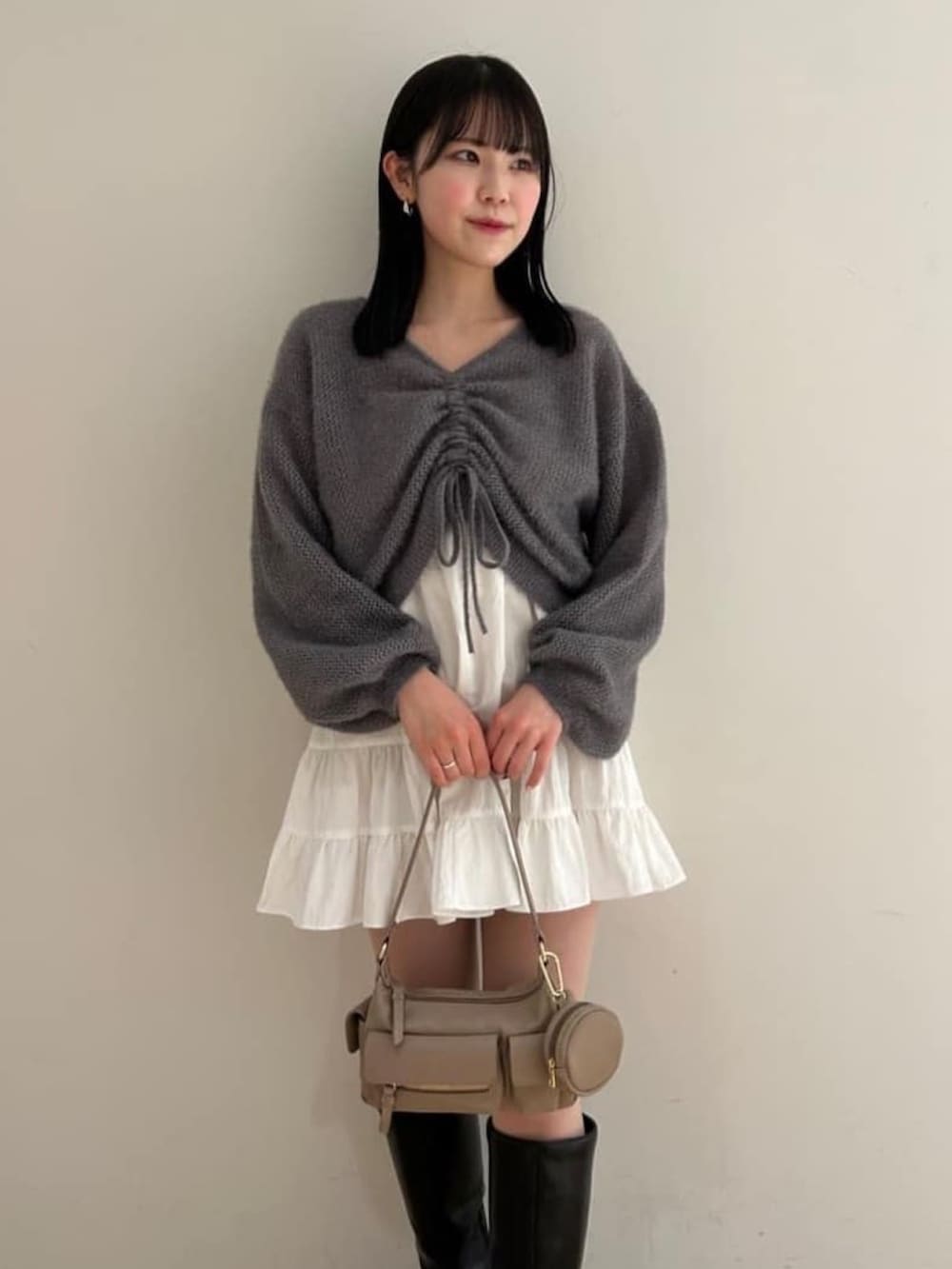 グレー系のニット/セーター、ホワイト系のワンピース、ブラック系のブーツを着用したレディースの冬コーディネートの2枚目の写真