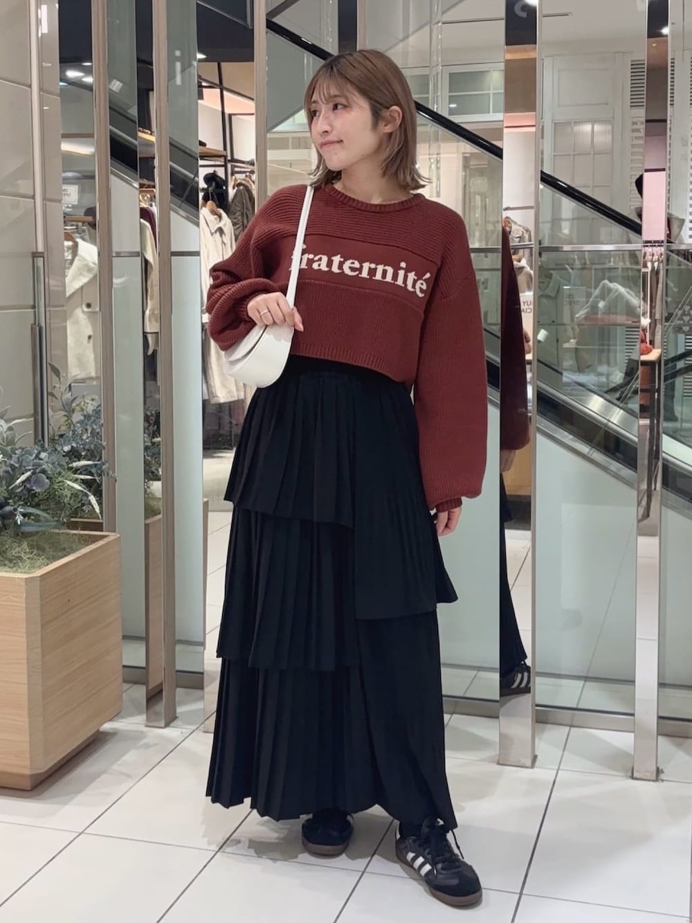 オレンジ系のニット/セーター、ブラック系のスカート、ホワイト系のマフラーを着用したレディースの冬コーディネートの2枚目の写真