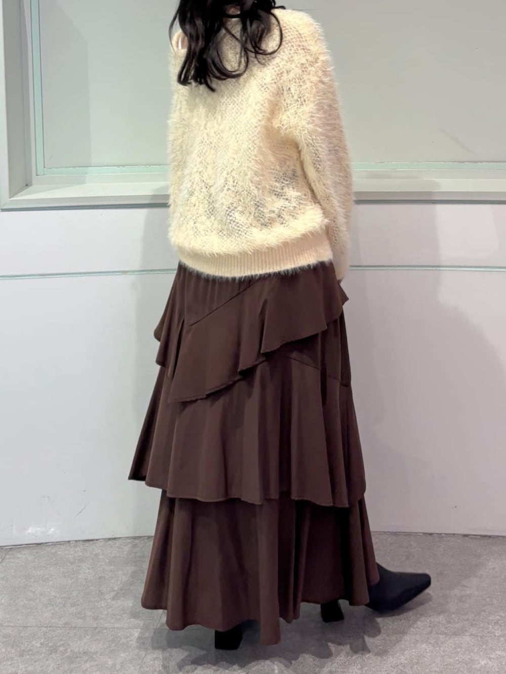 イエロー系のニット/セーター、ブラウン系のスカート、ブラック系のブーツを着用したレディースの秋コーディネートの3枚目の写真