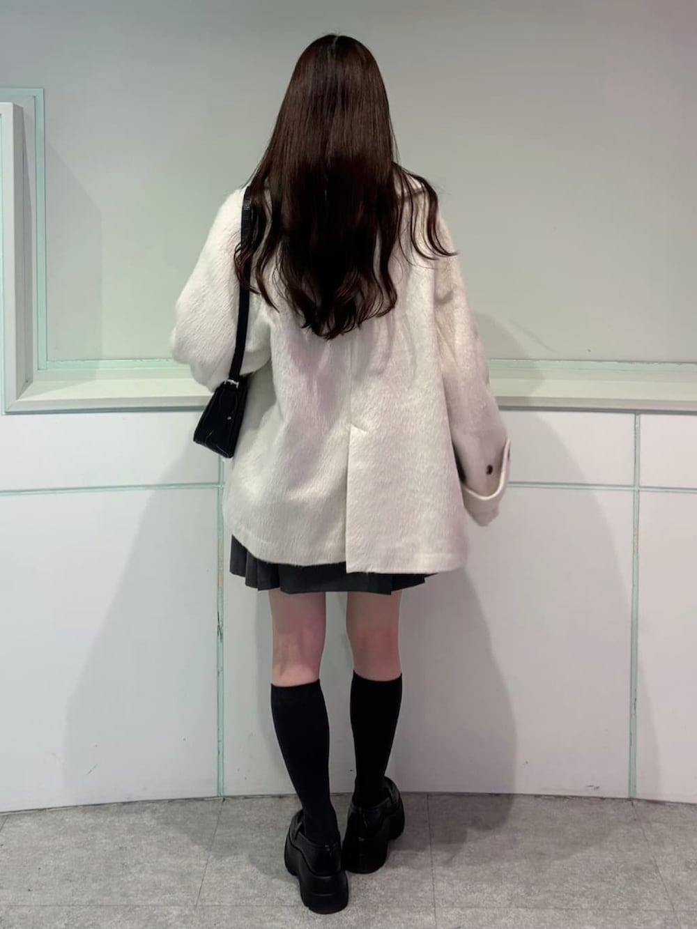 ホワイト系のチェスターコート、グレー系のスカート、ブルー系のニット/セーターを着用したレディースの秋コーディネートの2枚目の写真